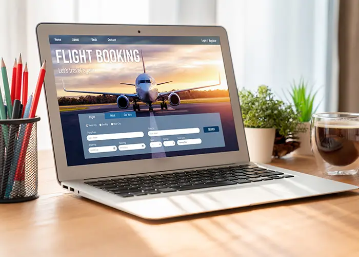 Laptop on desk displaying flight booking website with cup of coffee beside it