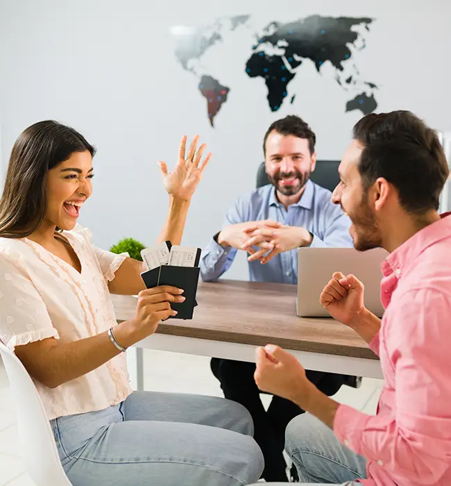 Three individuals at a table, one gesturing excitedly, with a world map in the background in a travel agency office.