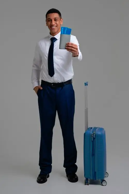 a traveller in business attire holding a passport and ticket next to a blue suitcase