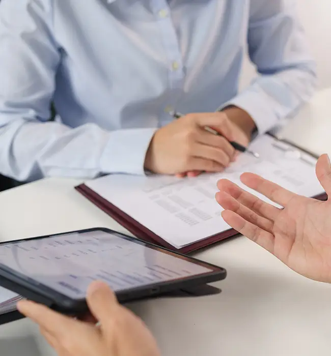 Person handing over a passport and a document with photos to another person across a desk with two stamps.