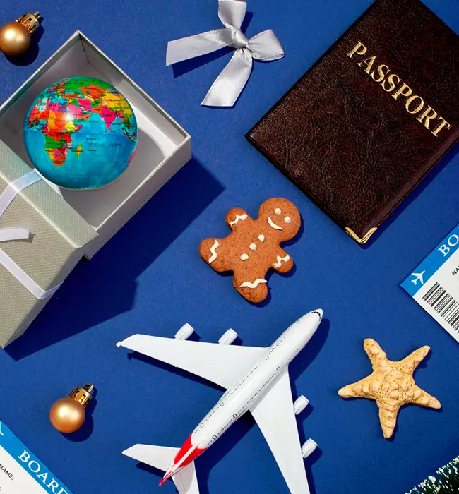 Travel-themed flat lay with passport, airplane model, globe, and gingerbread man on a blue background.