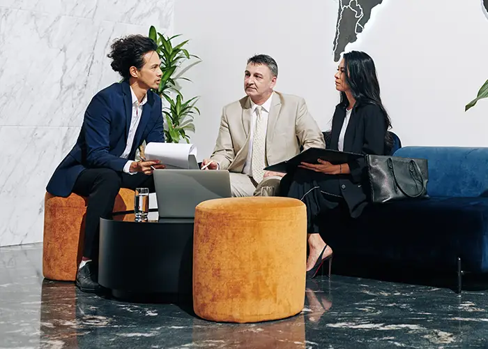 Three professionals in a modern travel agency lobby engaged in a discussion with a laptop.